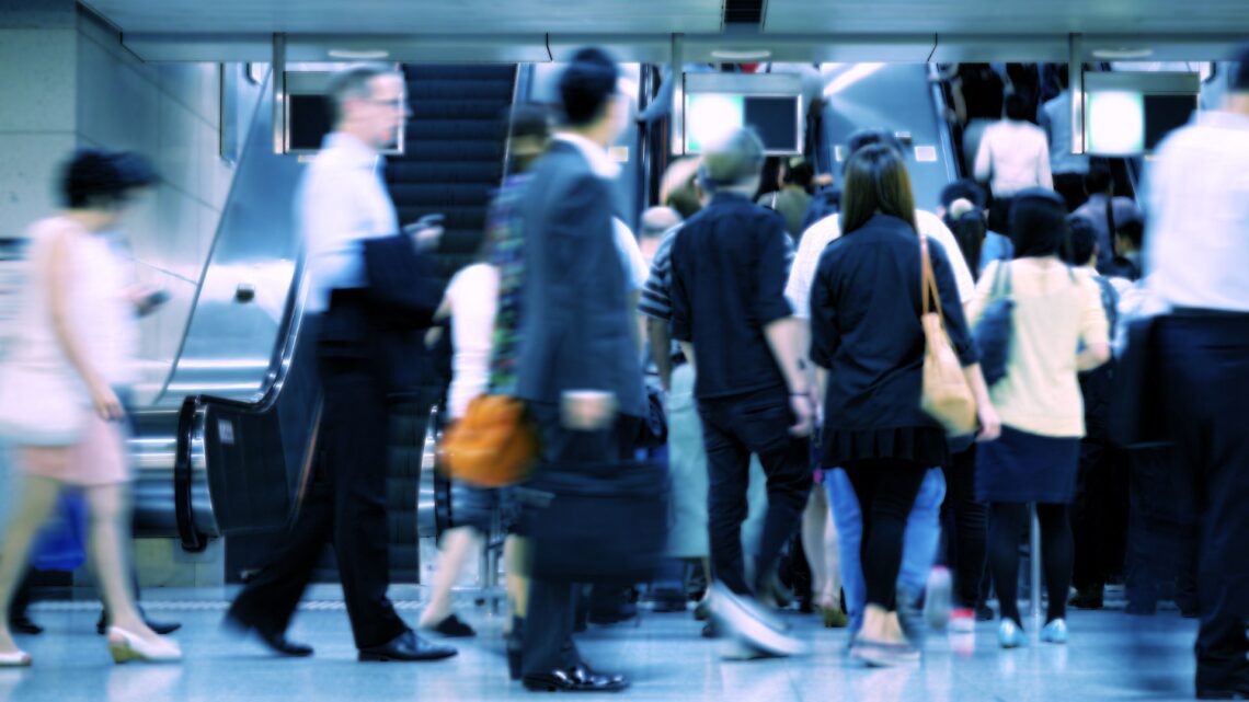 People moving through a busy train station with escalators and blurred motion.