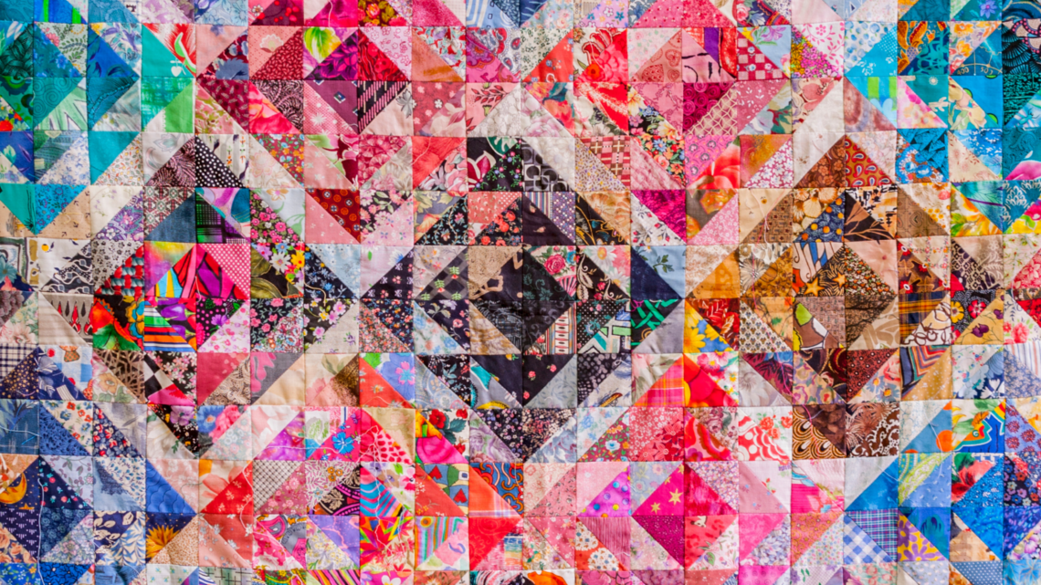 A colourful patchwork quilt made from many different patterned fabric pieces, forming heart shapes across the design.