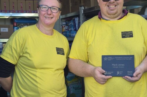 Mark Jones and Debbie Fretwell at The Hygiene Bank North Wales storage facility, standing beside shelves of donated hygiene products.